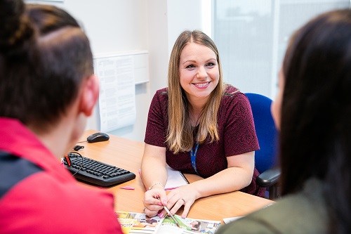 A female advisor sits behind a desk, smiling at two students.