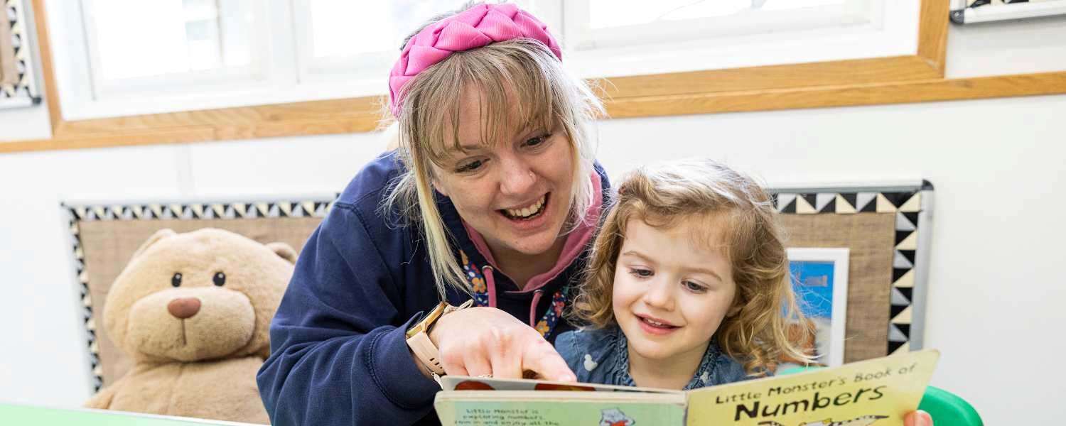 Female childcare apprentice reads to a young girl.