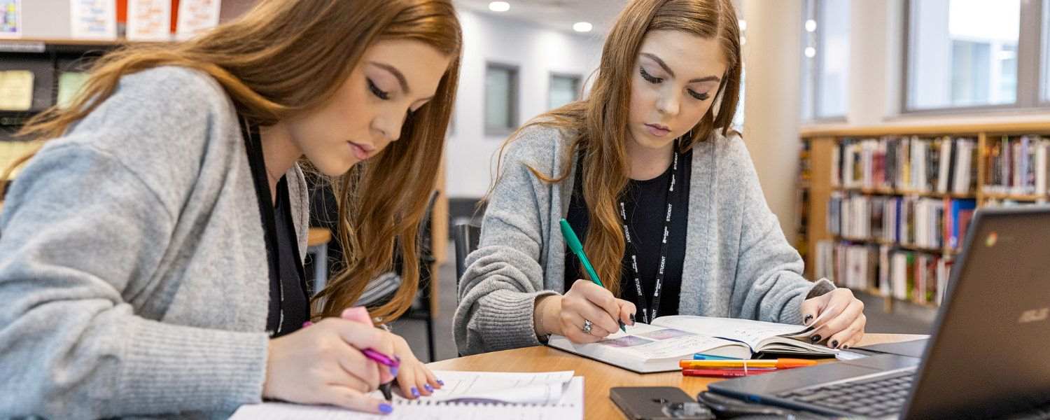 Two female students sit at a table, studying and highlighting notes together.
