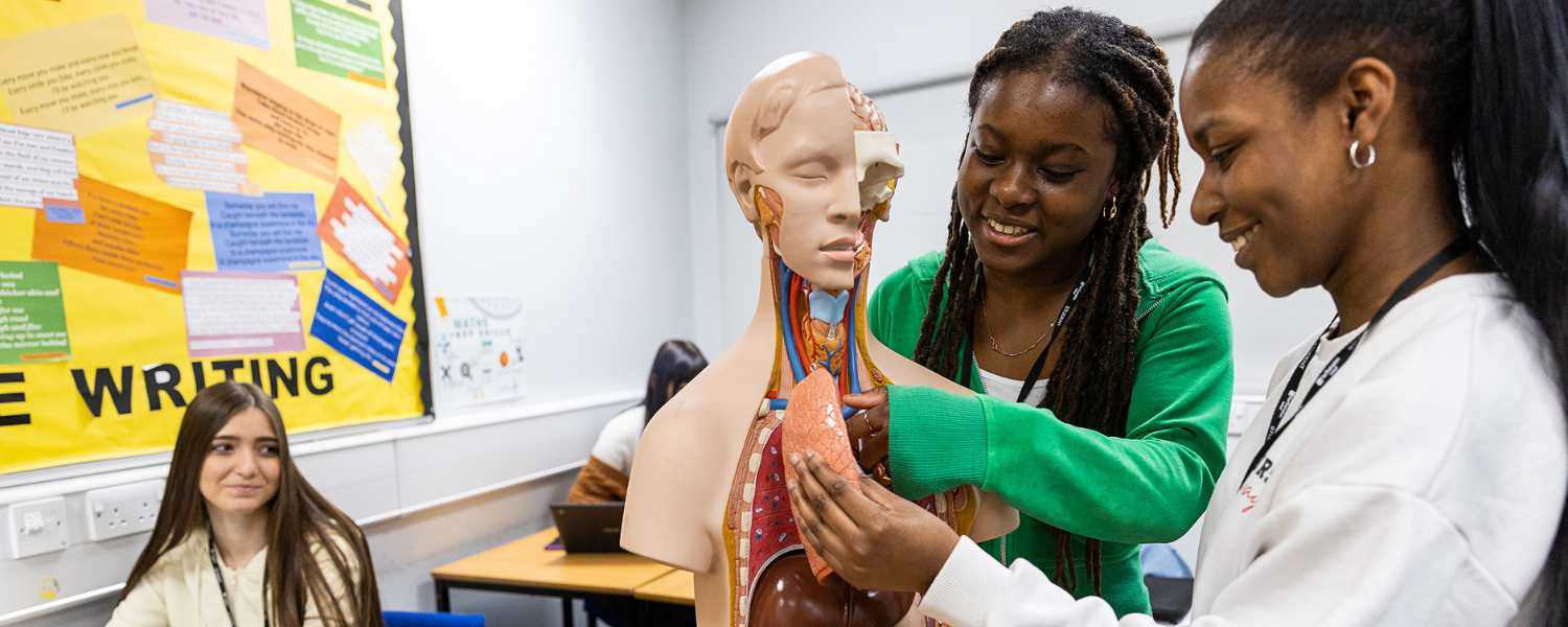 Two female students in a classroom, working on a health manikin. 