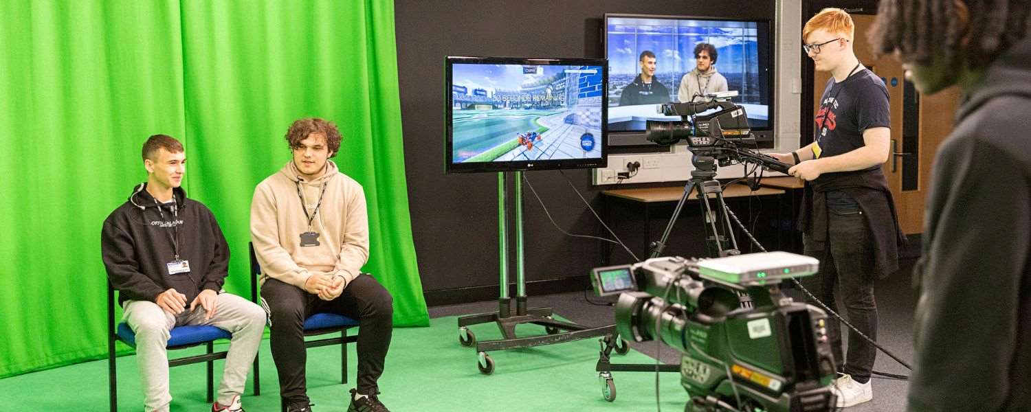 Two male students sit in front of a green screen in the College's TV studio.