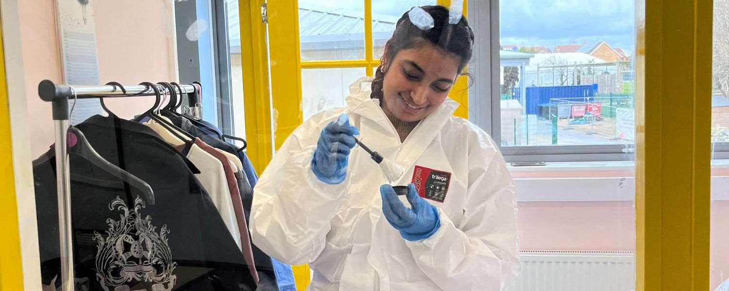 A female student, dressed in a hazmat suit, dusts for prints at a mock crime scene.