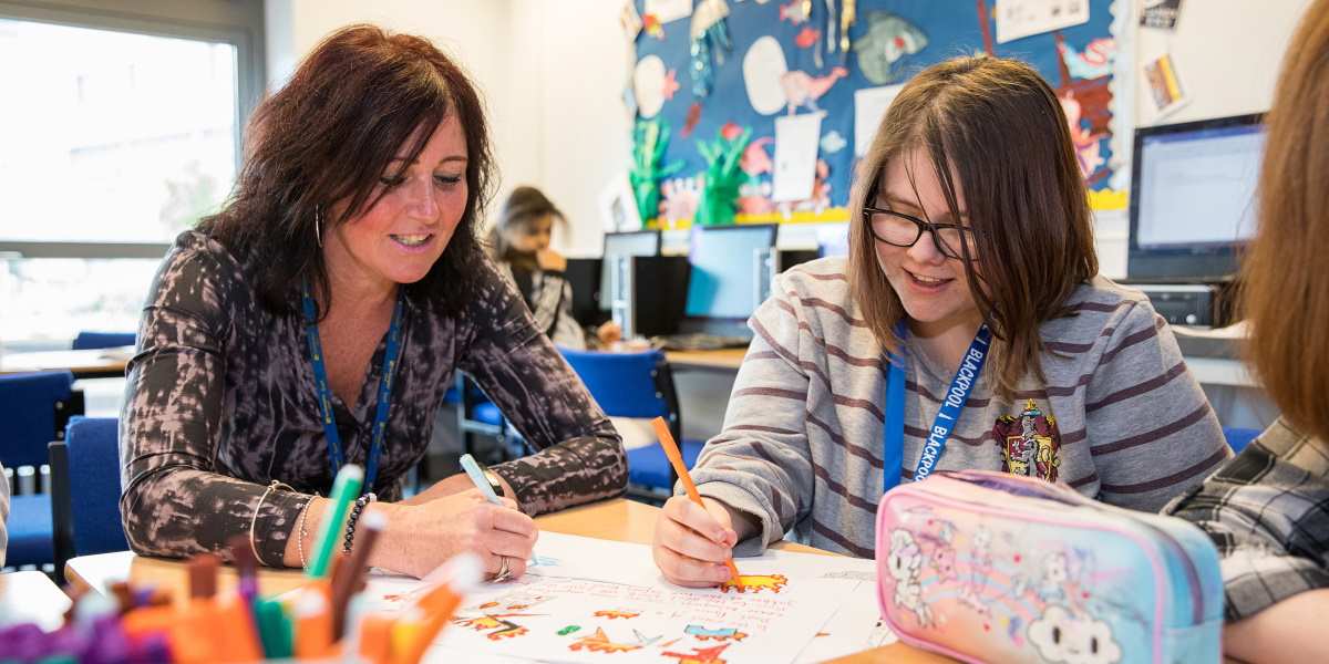 A female student and a female teacher work on a piece or art together.