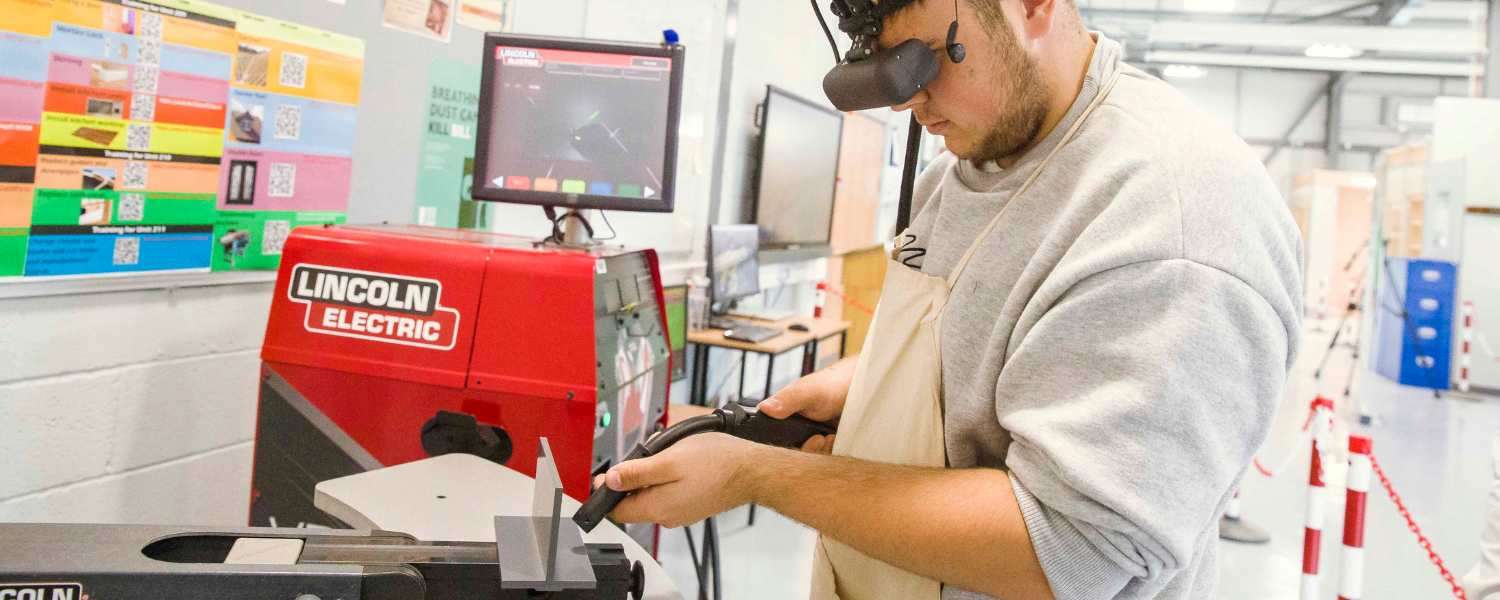 A male student in a workshop tries out a virtual welding simulation.