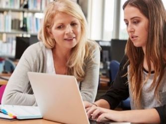 Two female adult students in a classroom, looking at a laptop