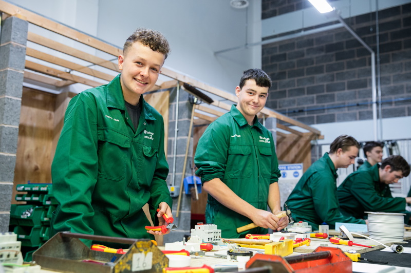 Two Electrical students smile while in a practical lesson.