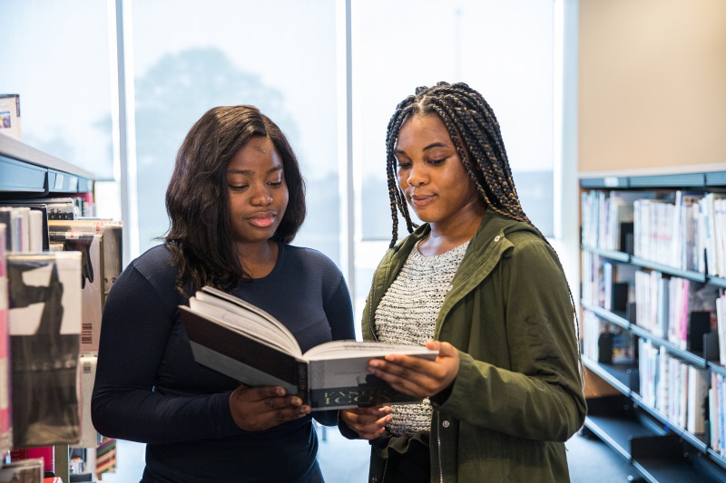 Two students read a book together in the College library.