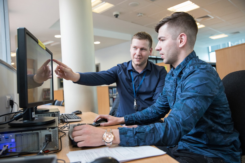 Member of staff helps a student on a computer