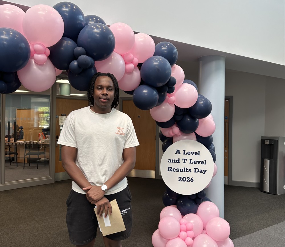Student stands in front of balloon arch with results.