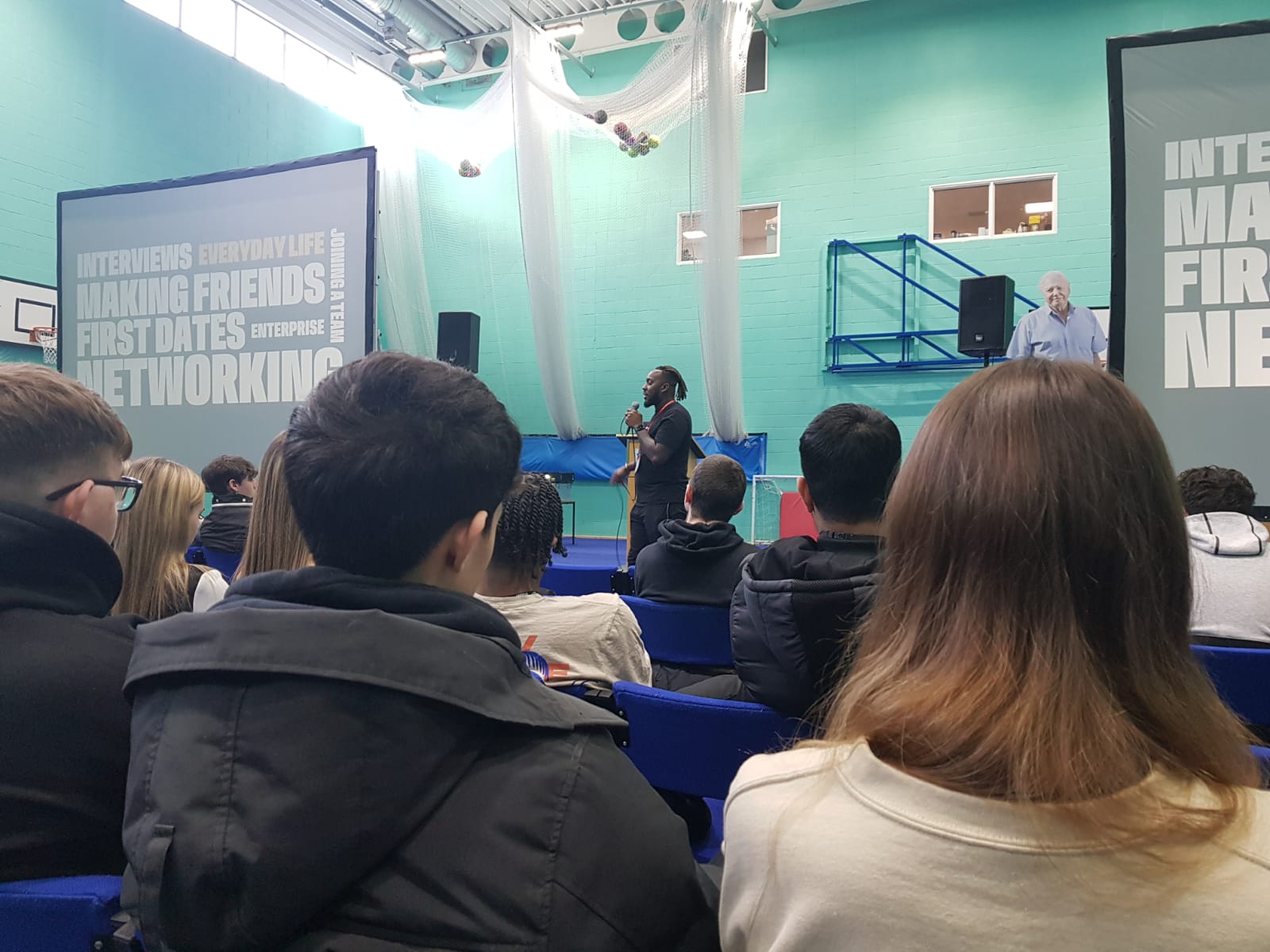 Students sitting in the Sports Hall in front of Loud Speaker colleagues, who are giving a speech