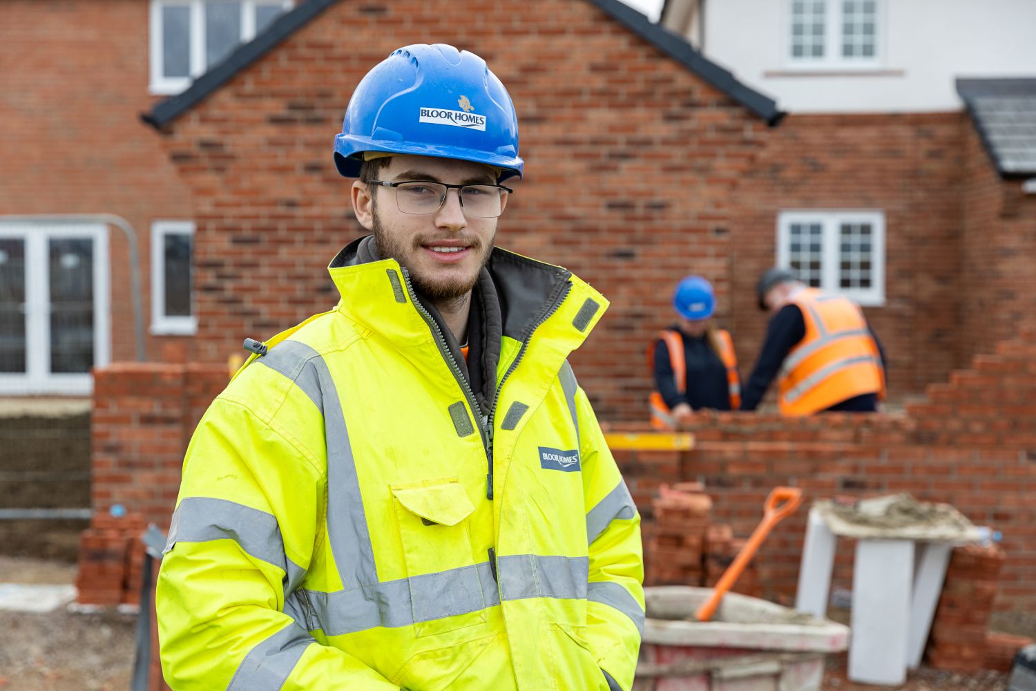 A manager and apprentice standing on a building site looking at bricks. 