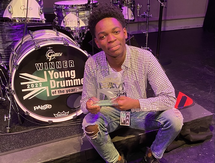 Jeremie on-stage next to his drums, holding his award trophy