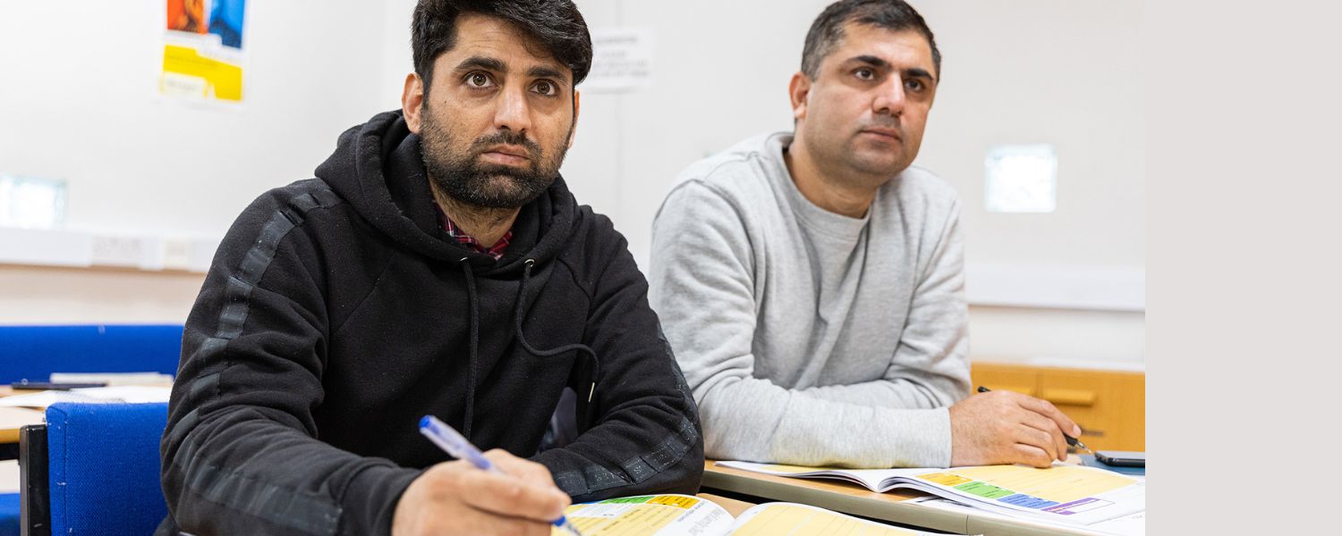 Two make students sit at a desk taking notes.