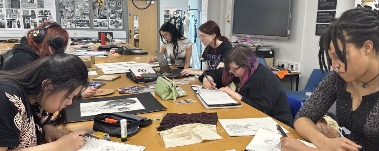 A group of students sitting in an art classroom together, working on a piece.
