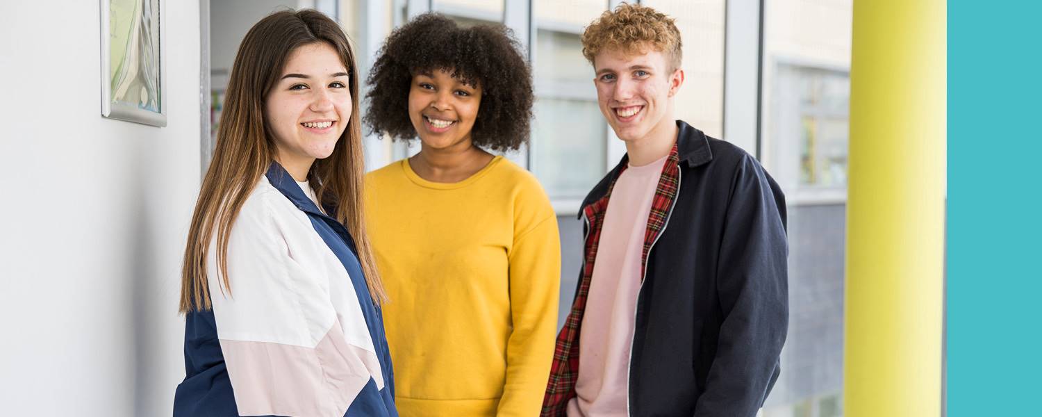 Image shows three students, two female and one male, smiling to camera.