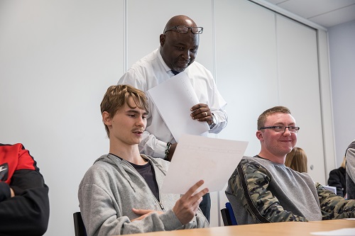 Image shows a teacher helping a student in a classroom.